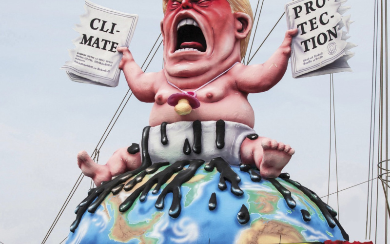 Eine Karikatur von Donald Trump zeigt diesen als Baby auf der Weltkugel sitzend, in der einen Hand ein Papier zu »Climate«, in der anderen ein Papier  zu »Protection«.  