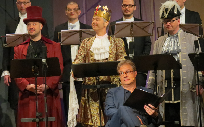 Several men in costumes read texts on a stage