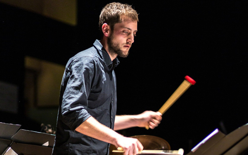 Young man with dark shirt plays on a percussion instrument.