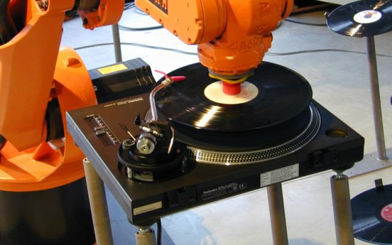 An orange robot arm puts on records.