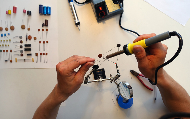 You can see hands from above that are holding a soldering iron. The person is soldering some wires together using a estra hand..