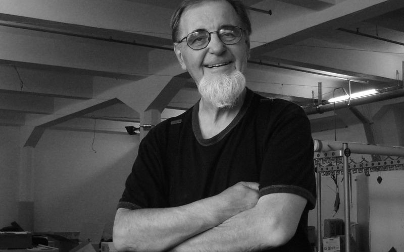 Portrait of Woody Vasulka in black and white: He stands, arms crossed, in his guest artist studio.