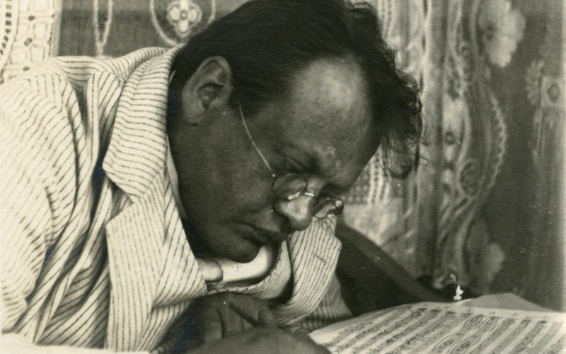 In einer alten schwarz-weiß Fotografie sieht man den Komponisten Max Reger am Tisch gebeugt über Notenblättern sitzen, einen Federhalter in der Hand.