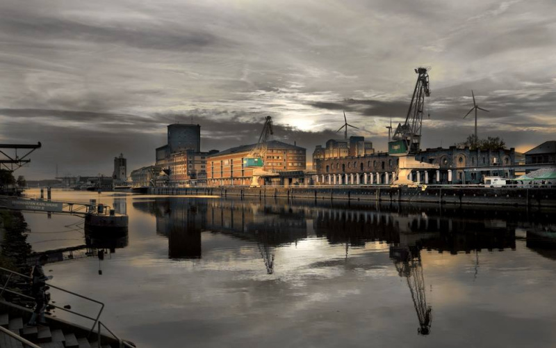 The photo shows illuminated industrial buildings along the Rhine. The sky is in gloomy evening mood.