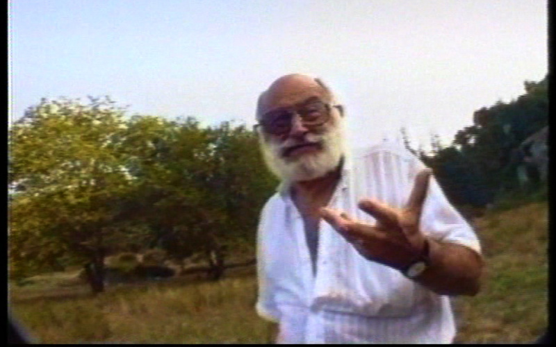 Mean with beard in a white shirt talks into the camera. It is Vilém Flusser