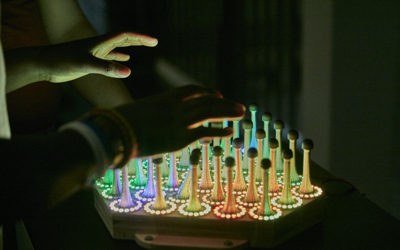 Hände über dem Werk »Wobble Garden«, dass aus Metallfedern und LED Kreisen besteht.