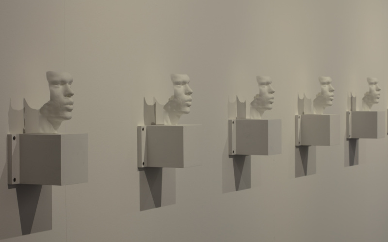  Several busts - 3D prints of the artists' vocal bands - hang side by side on a wall.
