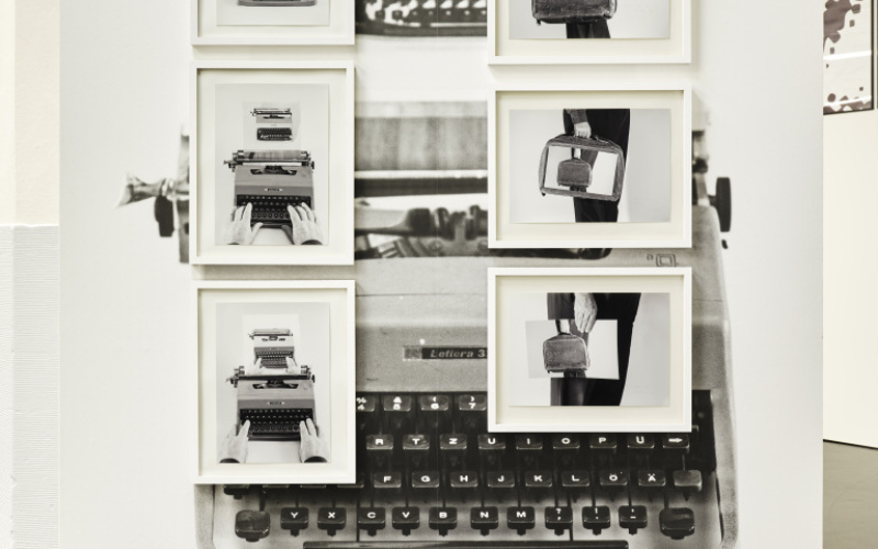 Das Foto zeigt eine schwarz weiße Fotocollage. Der Hintergrund wird von einer alten Schreibmaschine gebildet und auf dieser hängen 6 gerahmte schwarz/weiß Bilder die abwechseln eine Aktentasche und eine Schreibmaschine zeigen.