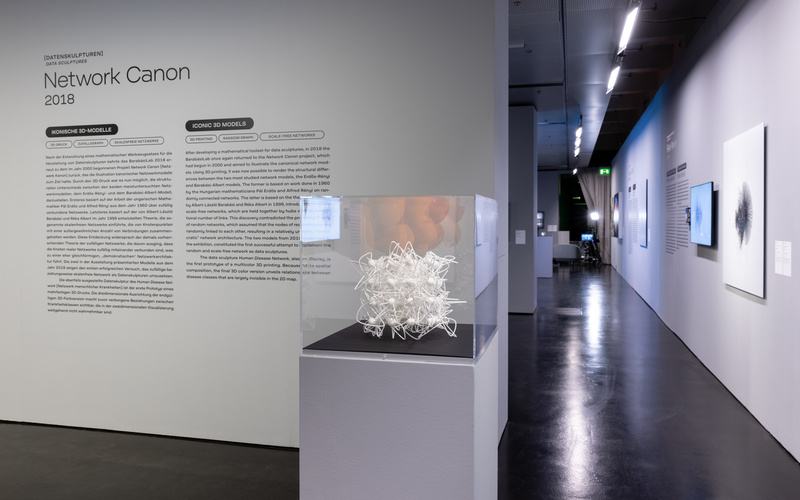 Ein Ausstellungsraum mit einem weißen 3D-Netzwerk-Modell in einem Glaskasten.