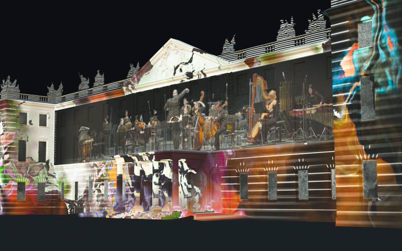 Auf der Karlsruher Schlossfassade ist ein Projection Mapping zu sehen, das in der Nacht leuchtet. Das Mapping zeigt bunte Farbwirbel, in deren Mitte ein Orchester spielt.