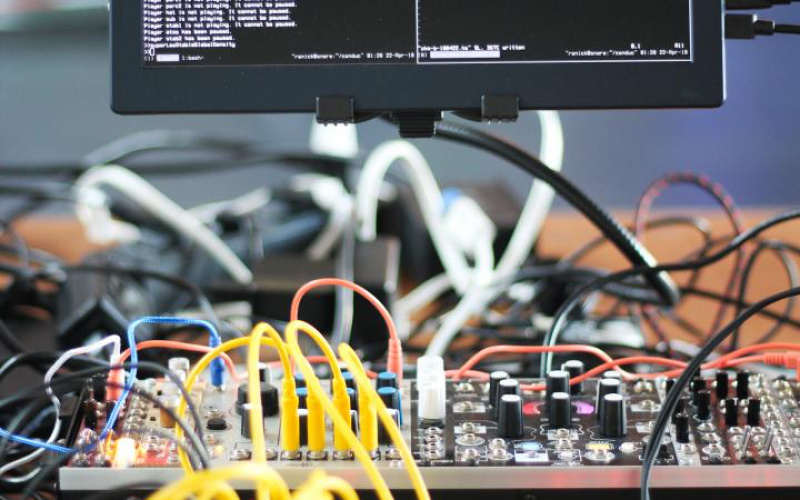 Code is shown on a display. Below is a console with coloured cables on a table.