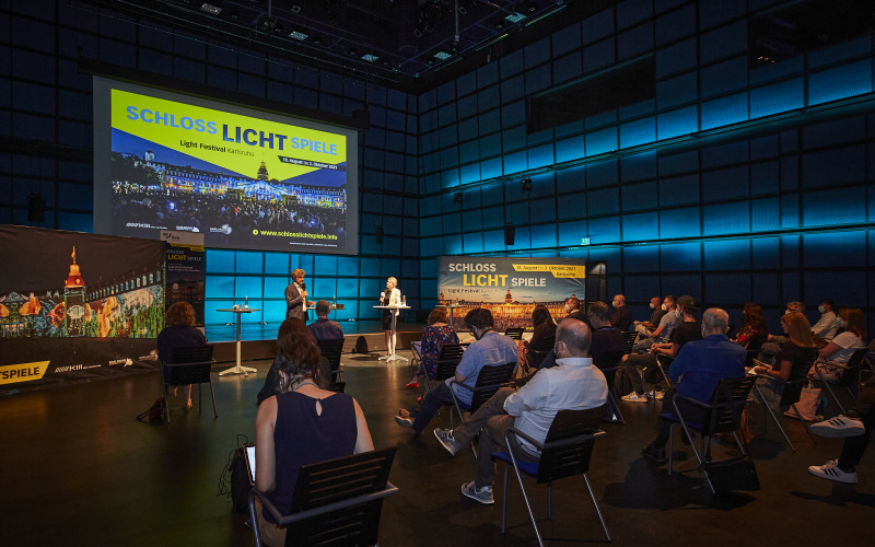 Die Pressekonferenz der Schlosslichtspiele 2021 im Medientheater des ZKM. Dominika Szope spricht zu Oberbrügermeister Dr. Frank Mentrup, Menschen sitzen im Publikum.