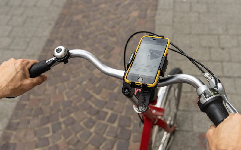 Zu sehen ist ein Ausschnitt von einem Fahrrad mit einem Handy auf der Handy-Halterung am Lenkrad.