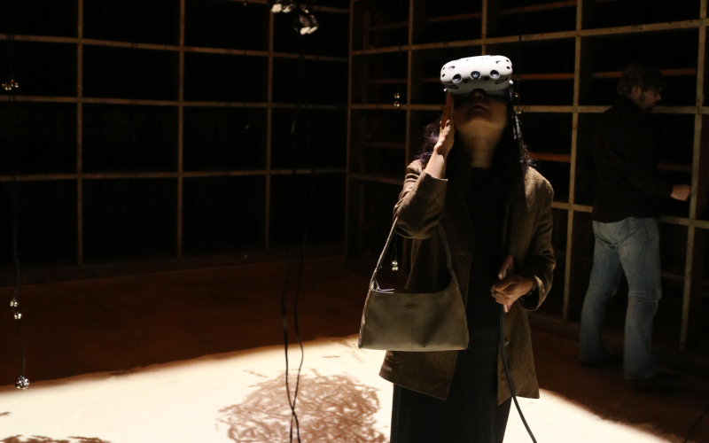 A visitor in a darkened room looks up at the ceiling through VR glasses.