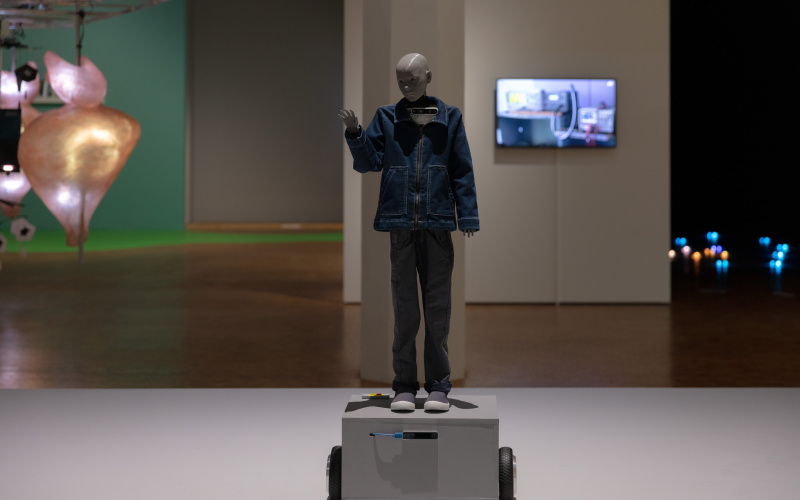 Anna Dumitriu & Alex May, »Cyberspecies Proximity«, 2020. In the picture there is a human-like robot raising his hand. He is wearing jeans clothes.