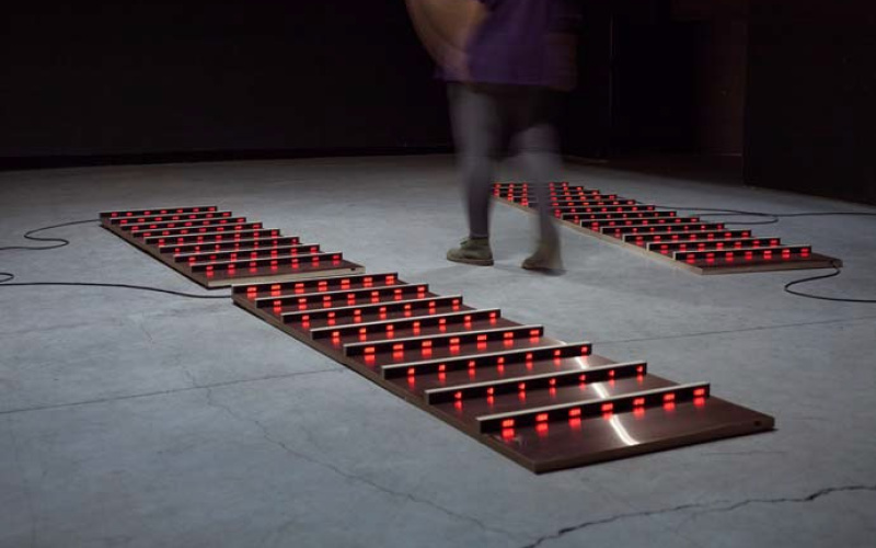 Exhibition view of the work »Patterns of Heat«, , plates lying on the floor with red luminous crossbars.