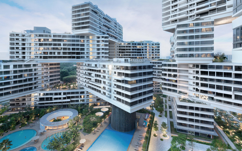 A large, modern and complex building runs through the picture. At the bottom of the picture is a courtyard with pool facilities and lawn. Behind it rises the multi-storey building. It consists of many winding blocks.