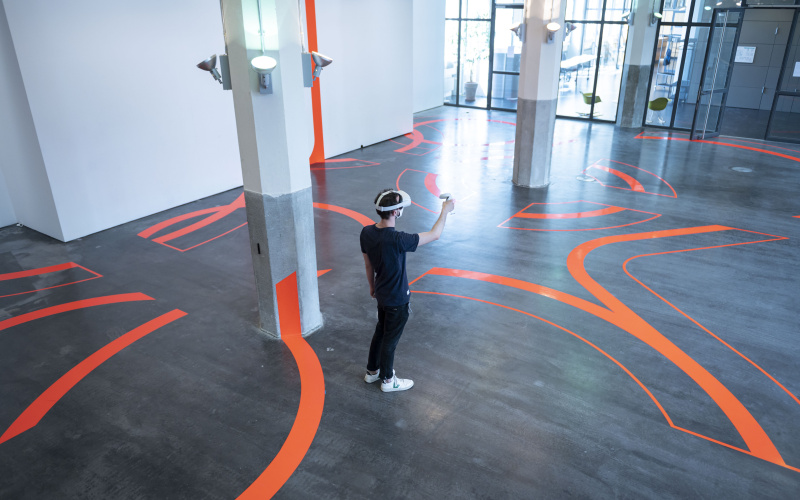 Ein Mann trägt eine VR-Brille und steht inmitten dicker Linien, die auf den Boden und auf die Wände geklebt sind.