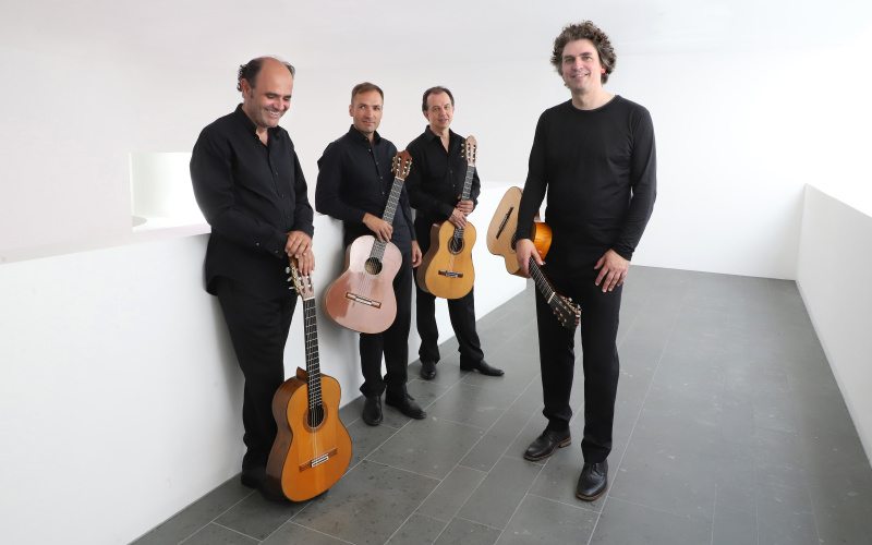 Auf dem Foto zu sehen, sind vier Männer, die in schwarz gekleidet sind und jeder hat eine Gitarre in seiner Hand. 