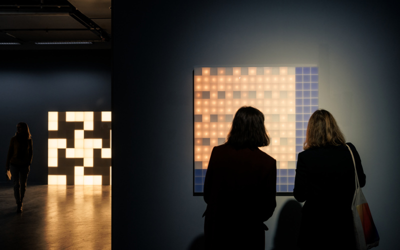 Two people are seen in front of a luminous Walter Giers work. In the background is another cube-shaped luminous object.