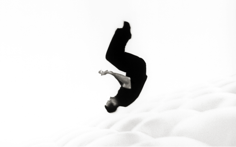 You can see a person dressed in black doing a roll in the air. The background is white.