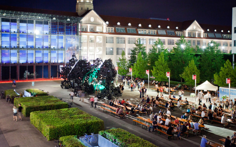 The ZKM forecourt bird's-eye view. It is evening. On display are many beer benches and food stalls.