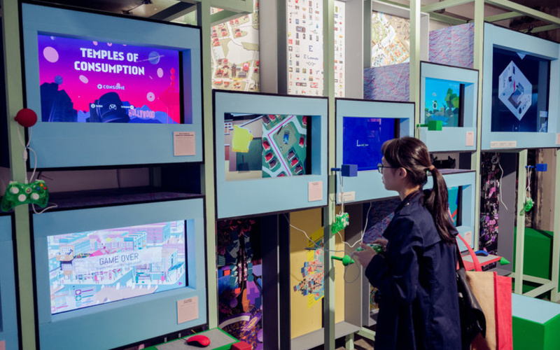 Person stands in front of several screens with a gaming controller