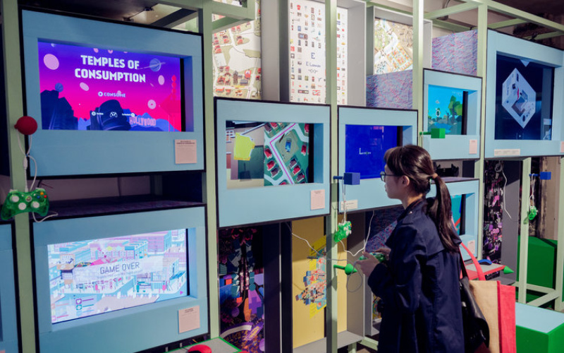 Person stands in front of several screens with a gaming controller