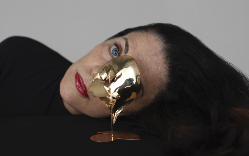 Analivia Cordairo can be seen tilting her head to the side. Her face is partially covered by a golden sculpture.