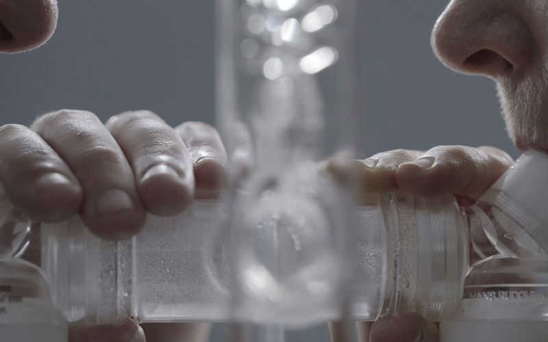 In the picture, there are two people blowing into a tube construction, one on the left and one on the right.