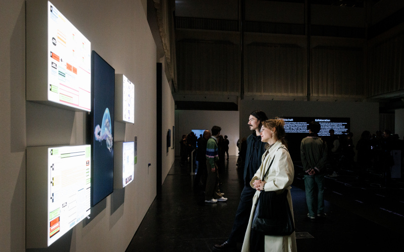 You can see two people looking at four small screens.