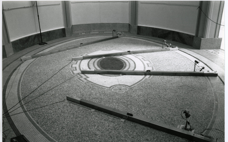 Man sieht das Werk »Number Made Audible«. Das schwarz-weiß Foto zeigt einen runden Raum. Auf dem Boden befinden sich vier lange Stelzen, an denen Kabel befestigt sind.