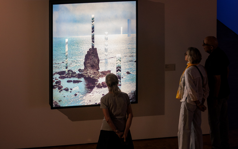 Three people can be seen looking at a work of art hanging on the wall. The artwork shows something reminiscent of an iceberg in the Arctic.