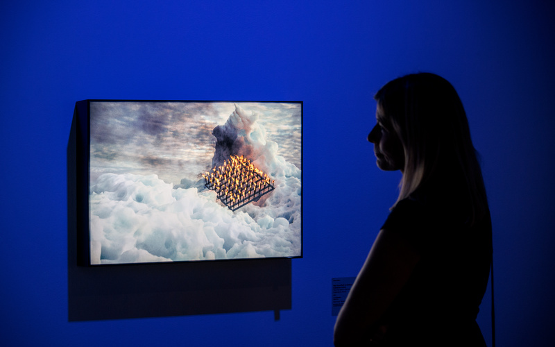 A work of art can be seen, which a young woman is looking at. The artwork shows an icy landscape with yellow lamps in the middle.