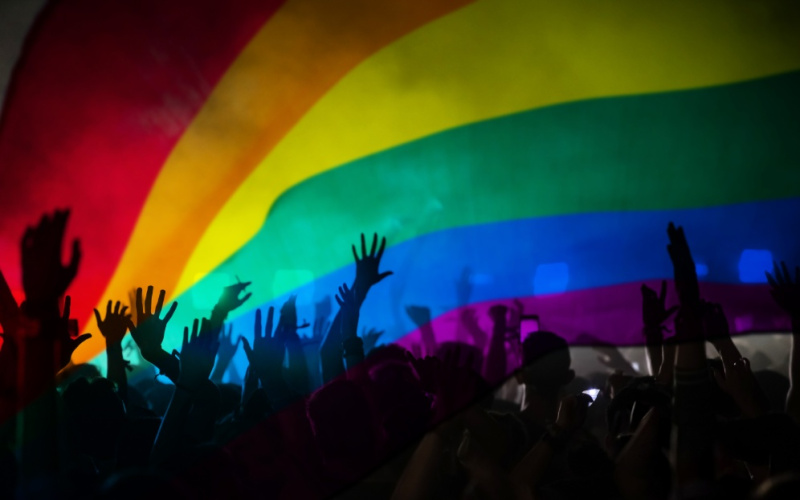 Hands can be seen in front of a rainbow flag.