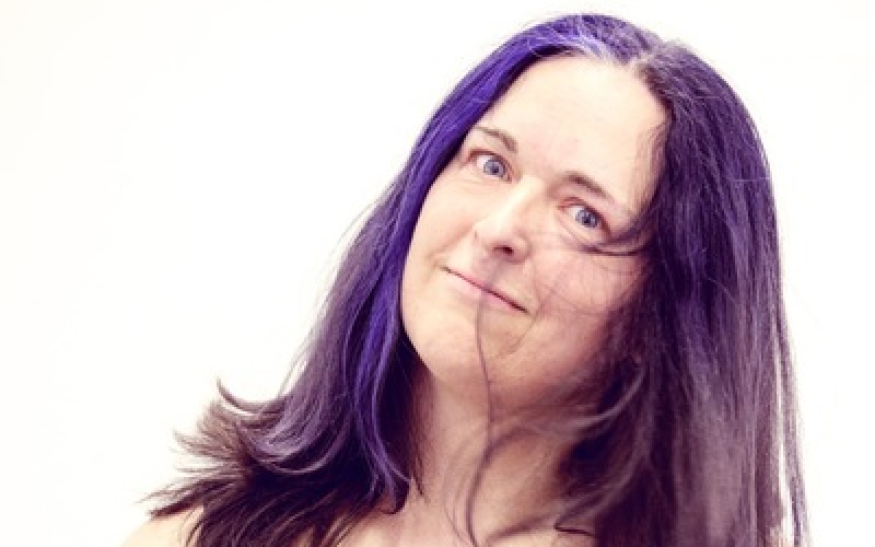 Woman with purple hair, holding her head at a slight angle.