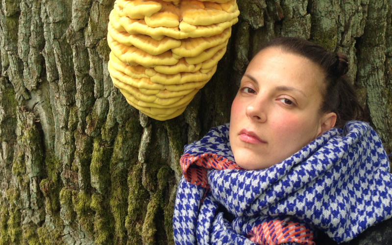 A woman with a blue and white checkered scarf poses next to a tree mushroom