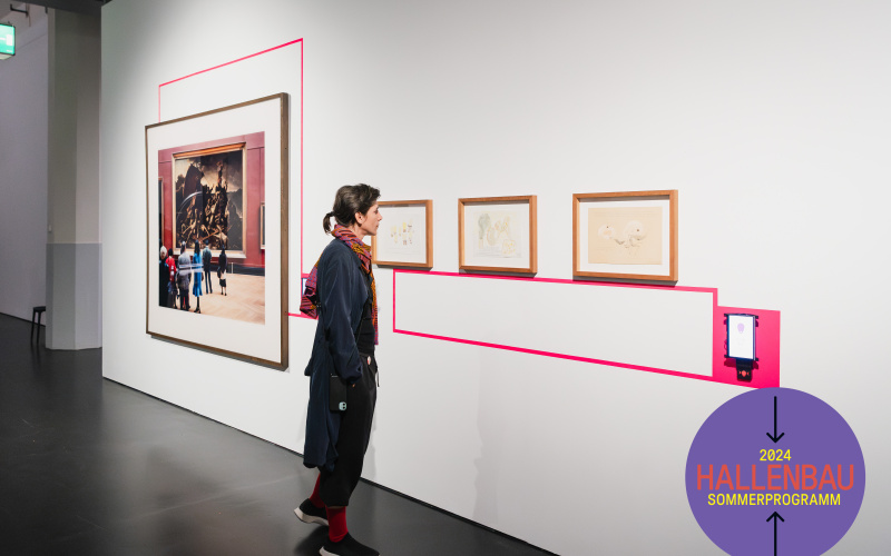 A woman in a coat looks at pictures on a white wall