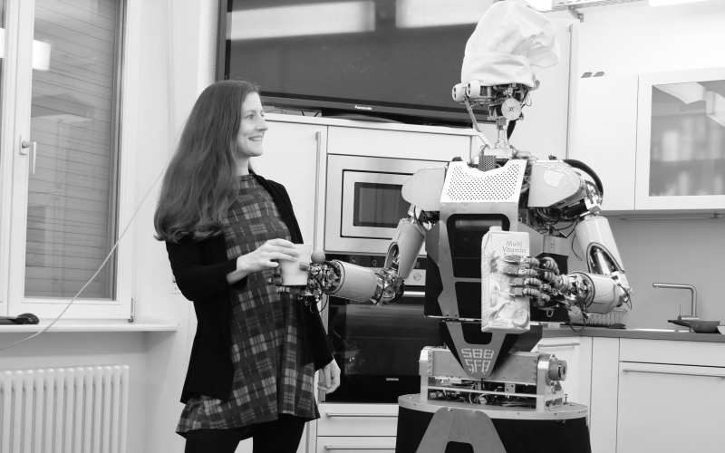 Black and white photograph of Franziska Krebs and a humanoid robot handing her a cup of juice. 