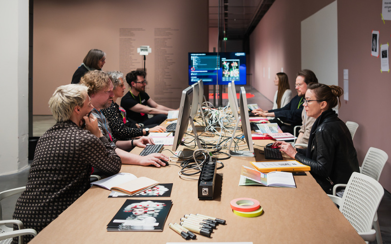 The picture shows several people working together on computers. 