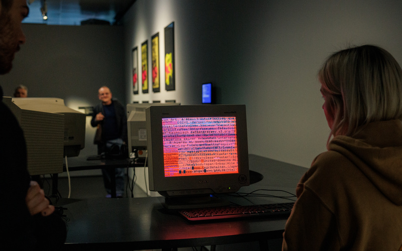 Eine Person schaut in einem dunklen Raum auf einen alten Computermonitor, auf dem Codezeilen auf rötlichem Hintergrund angezeigt werden.