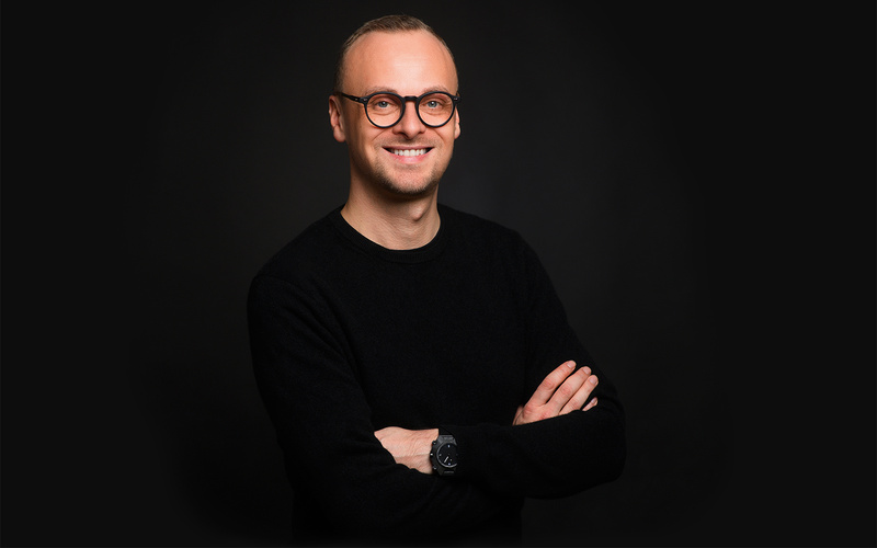 A portrait photo of a person with glasses against a black background. 