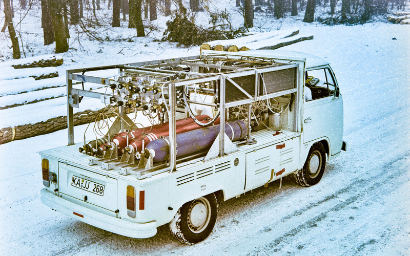 Zu sehen ist ein helles Auto, das auf einer schneebedeckten Straße steht.