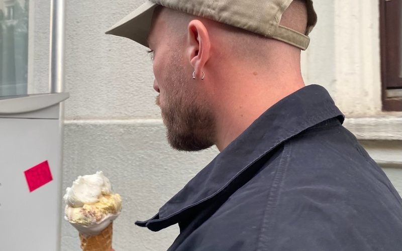 The picture shows a person holding an ice cream and wearing a cap. 