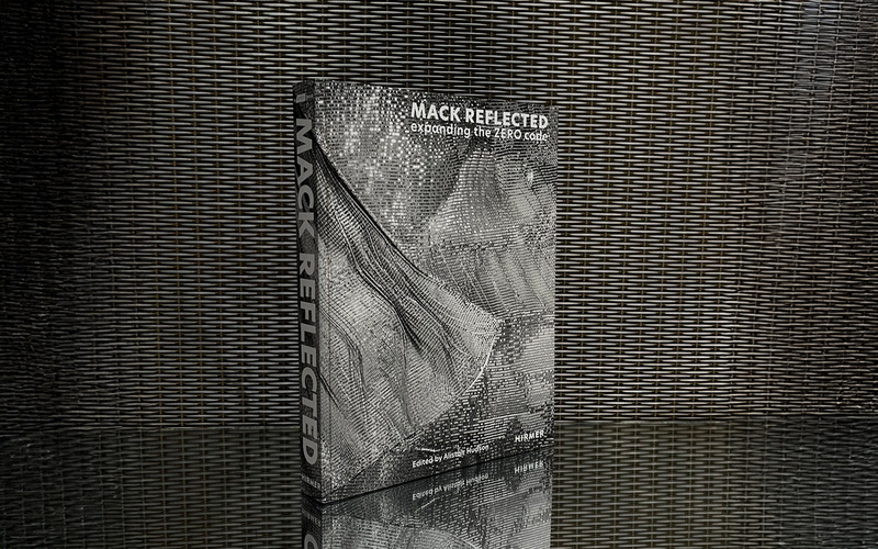 The image shows a book, standing on a reflective surface that reveals its mirror image.