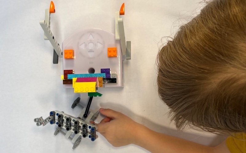 Ein Kind ist zu sehen, welches auf einem Blatt Papier zusammen mit dem Thymio-Roboter malt.