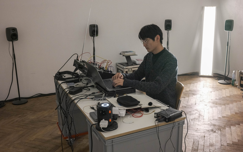 A person is sitting at a laptop surrounded by speakers.
