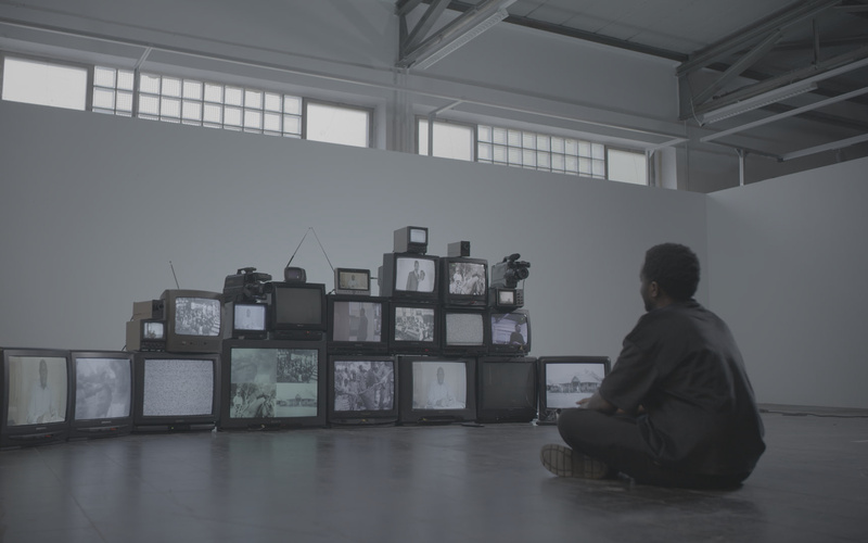 The picture shows a person sitting on the floor looking at an installation of old televisions.