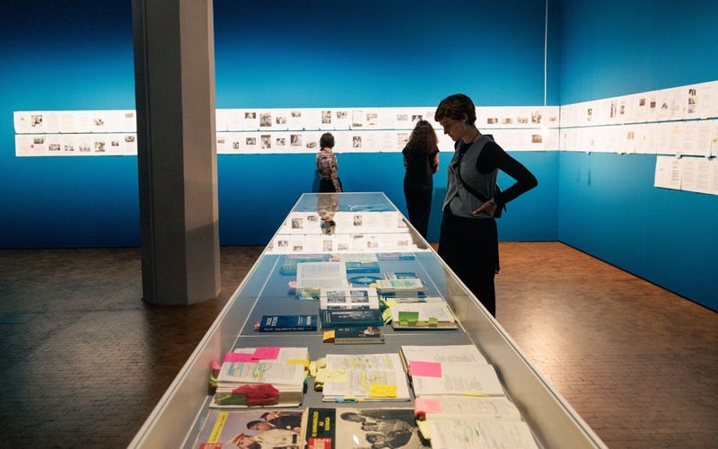 Zu sehen ist eine Person, die einen Ausstellungstisch mit Büchern betrachtet.