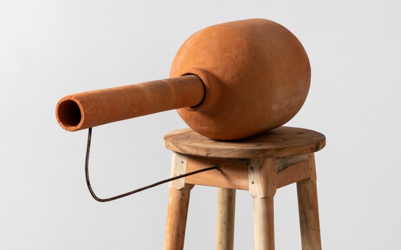 Ein Kunstwerk aus rotem Ton auf einem Holzhocker.